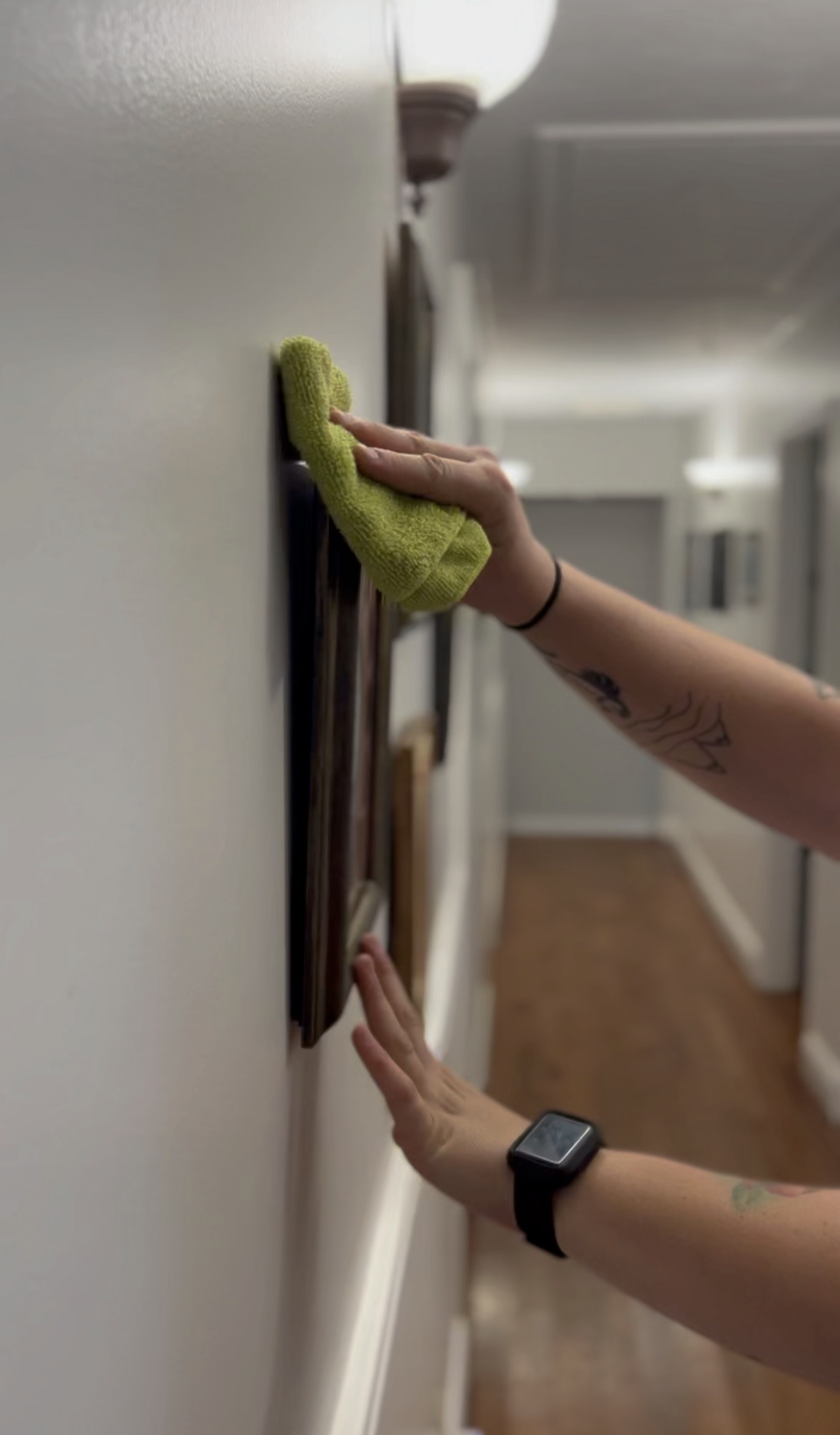 YFNCL cleaner carefully dusting framed wall art in a hallway with a green microfiber cloth